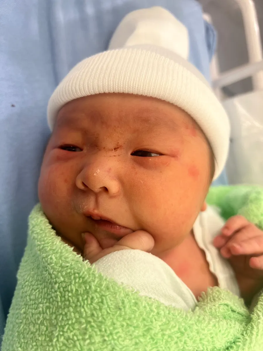 Newborn Amadeus in a white knit hat, swaddled in a green towel