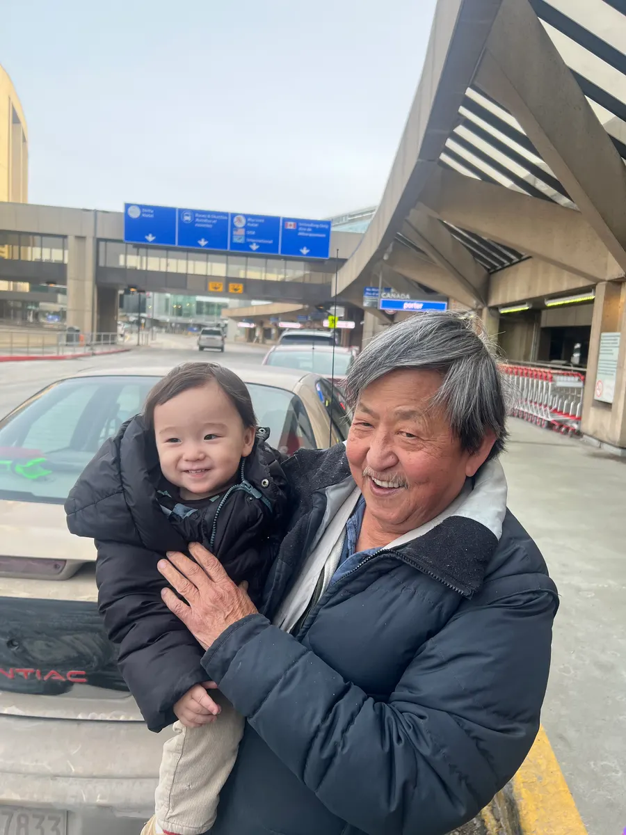 Amadeus at 13 months smiling in family's arms outside Calgary airport