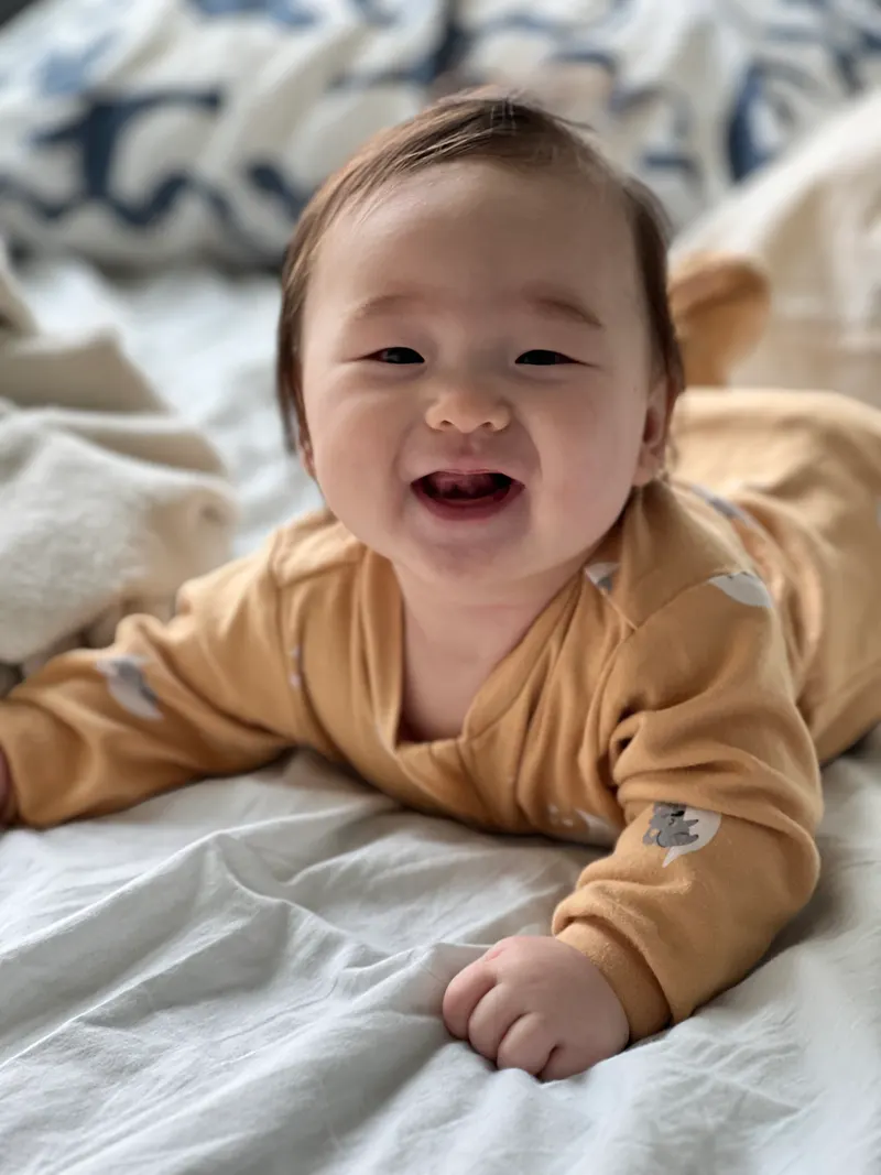 Amadeus at four months grinning on a bed in a mustard romper