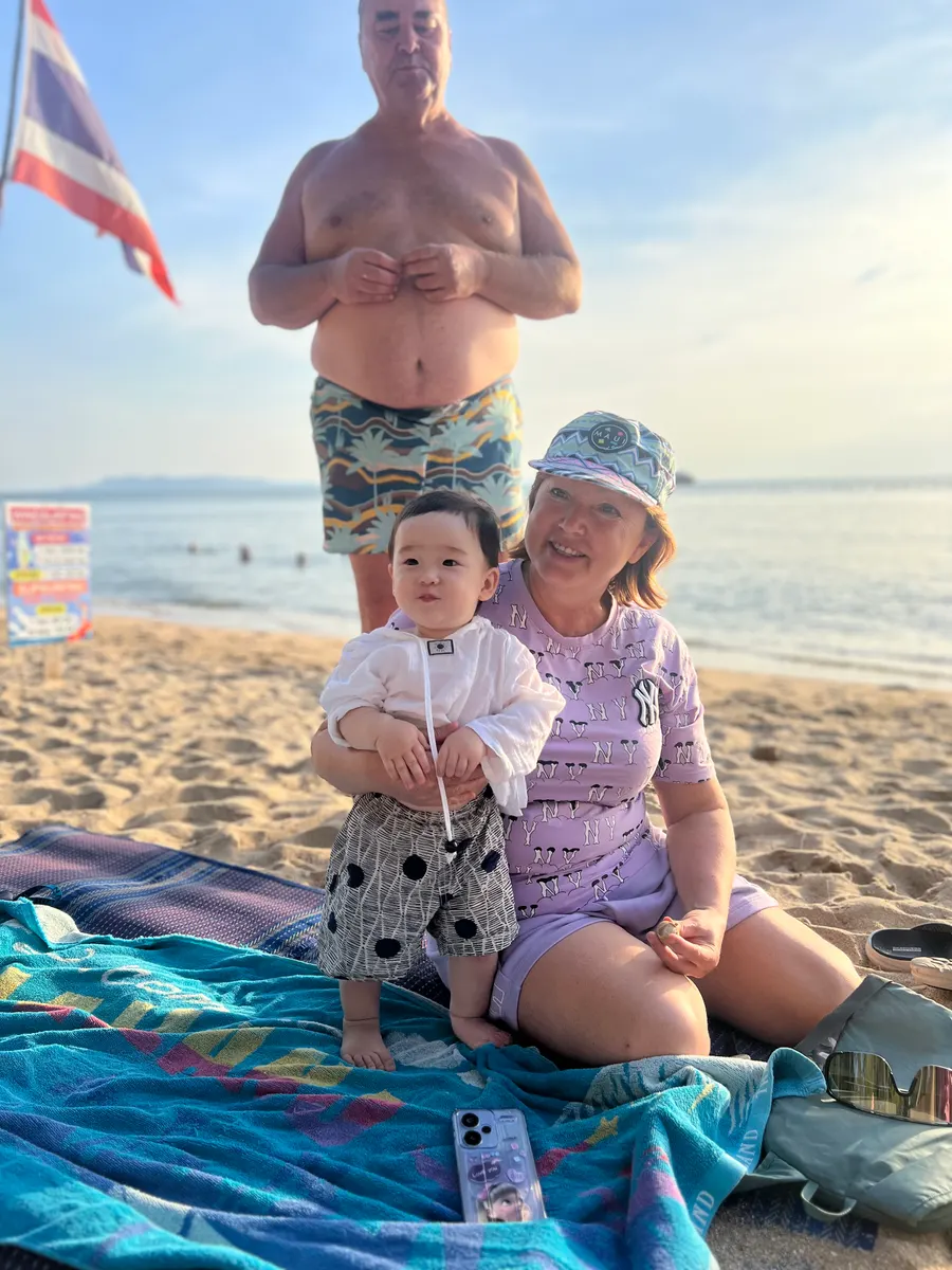 Amadeus at 12 months on a beach in Pattaya, Thailand, sitting on a towel with family