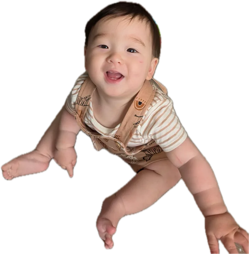 Amadeus at 16 months sitting on the floor in striped overalls, grinning